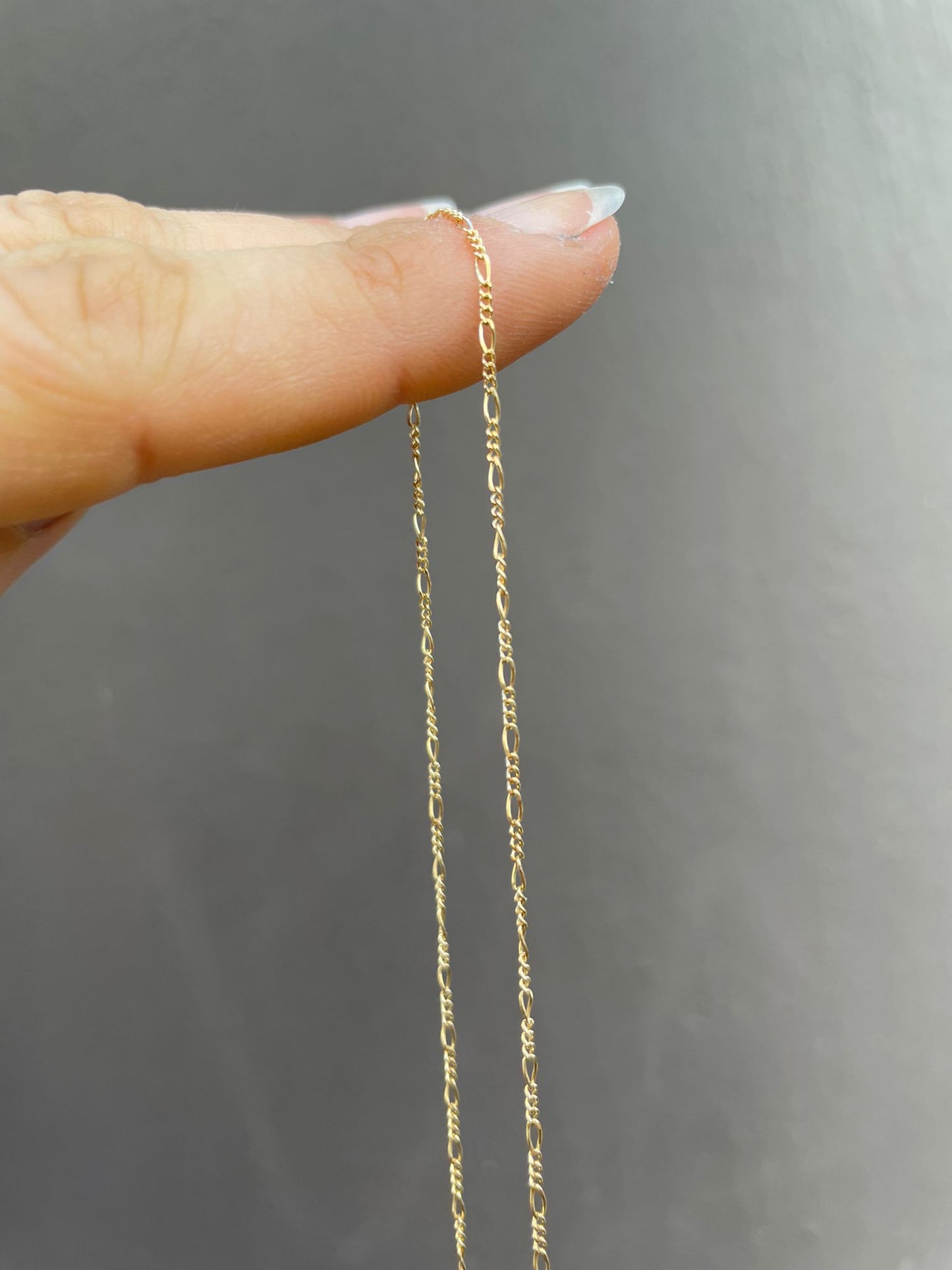 18 karat gold Figaro chain. The chain features an alternating pattern of elongated oval links and shorter round links. It is available in a variety of lengths.