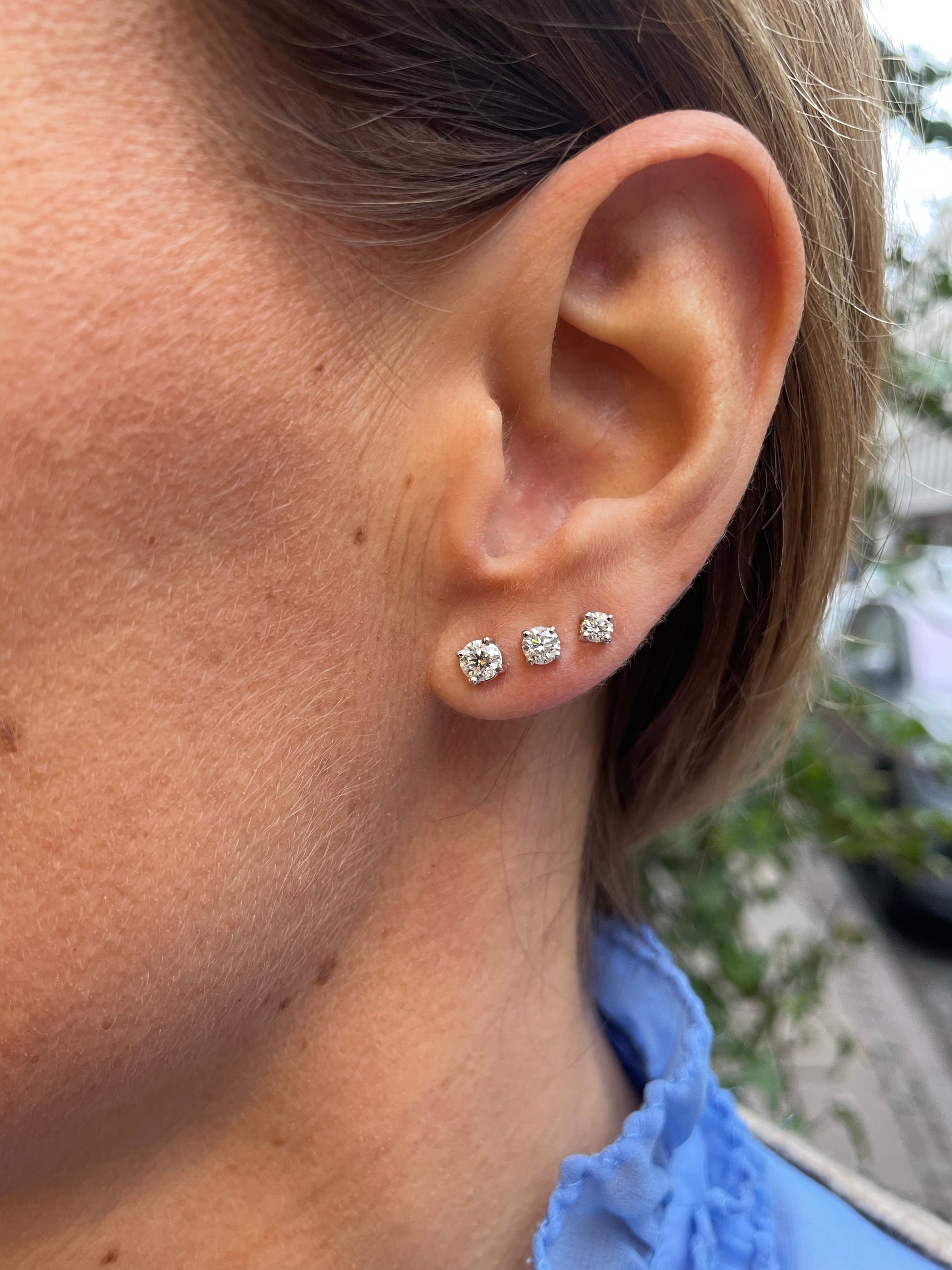 Three 18 Karat white gold earrings in an ear, each showcasing a different carat diamond.