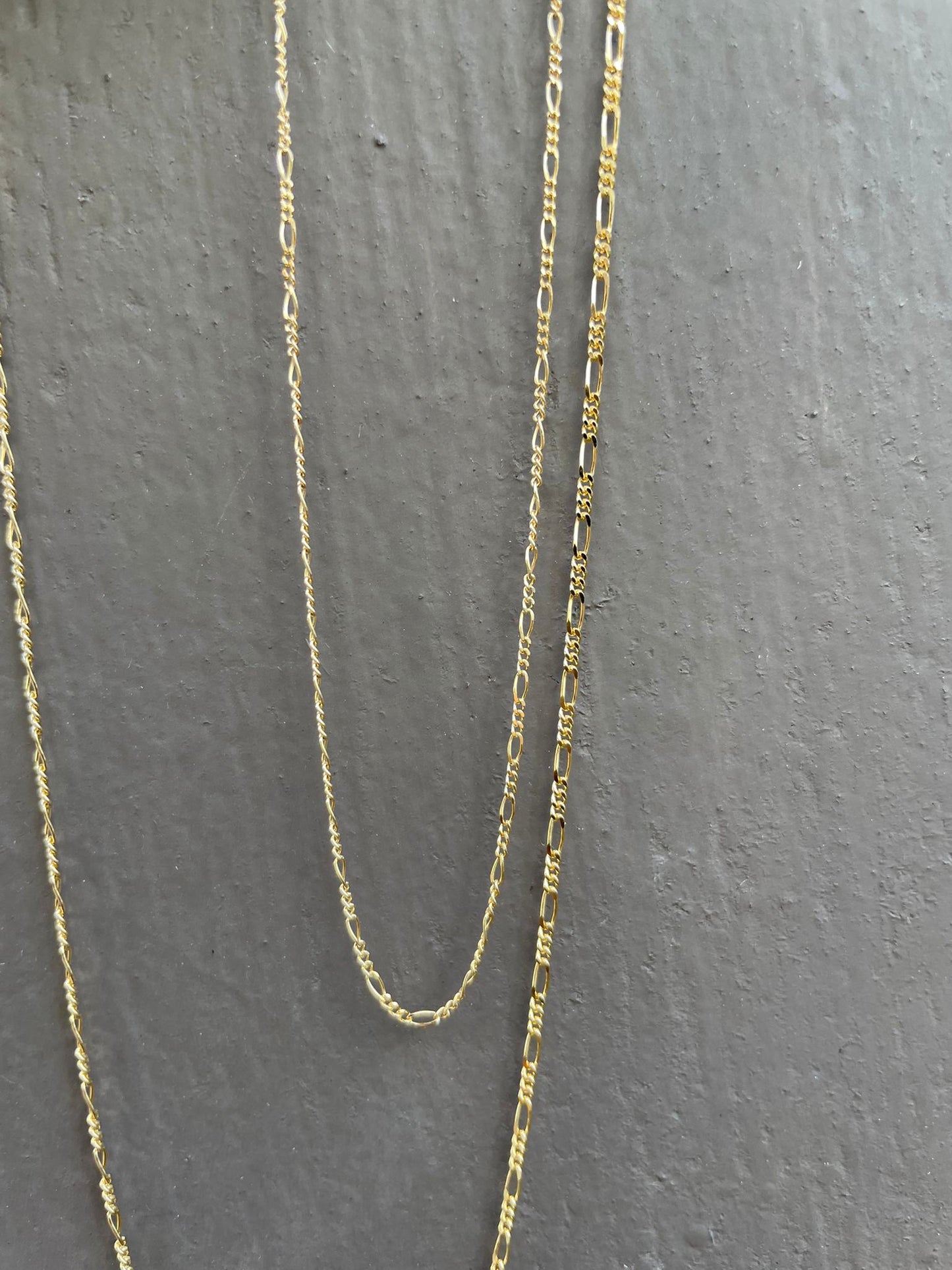 18 karat gold Figaro chain. The chain features an alternating pattern of elongated oval links and shorter round links. It is available in a variety of lengths.
