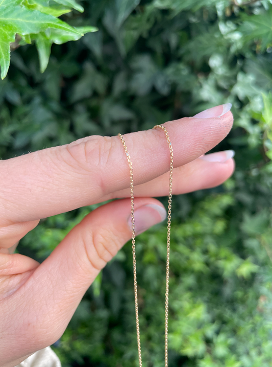 Closeup of a 18 karat gold ancherchain necklace being held by a hand.