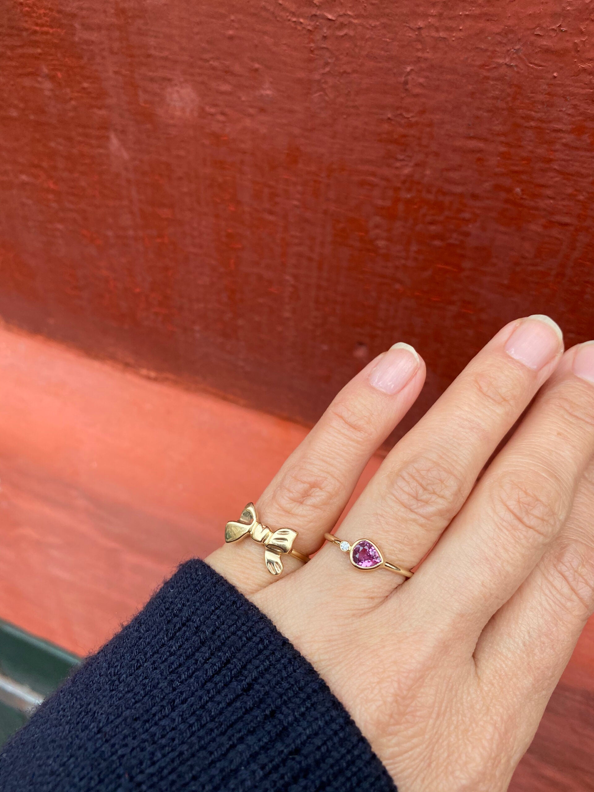 The picture features a pink sapphire ring in a brilliant cut. On the ring is also a round diamond. The ring is styled with a gold ring in the shape of a bow.